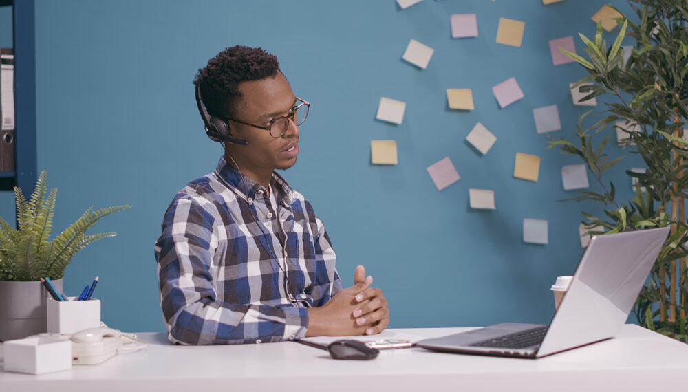 Helpline operator giving telemarketing assistance and support at client care call center, talking on phone call with people. Sales adviser using microphone and headphones at customer service.